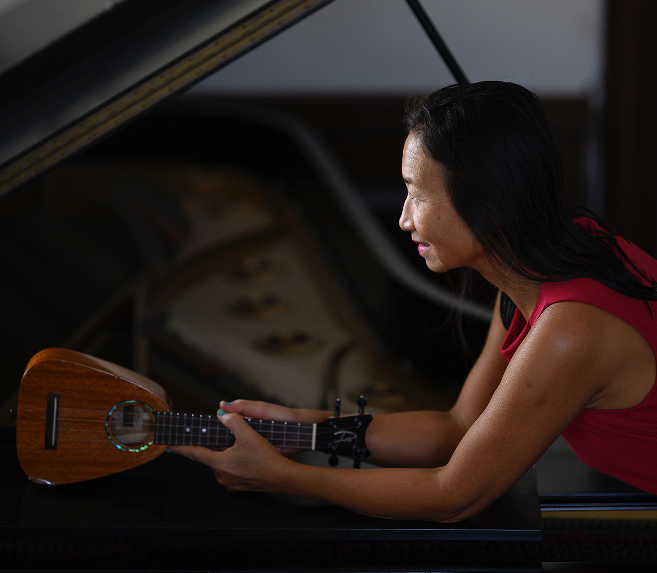 Woman holding a ukulele shown in profile.